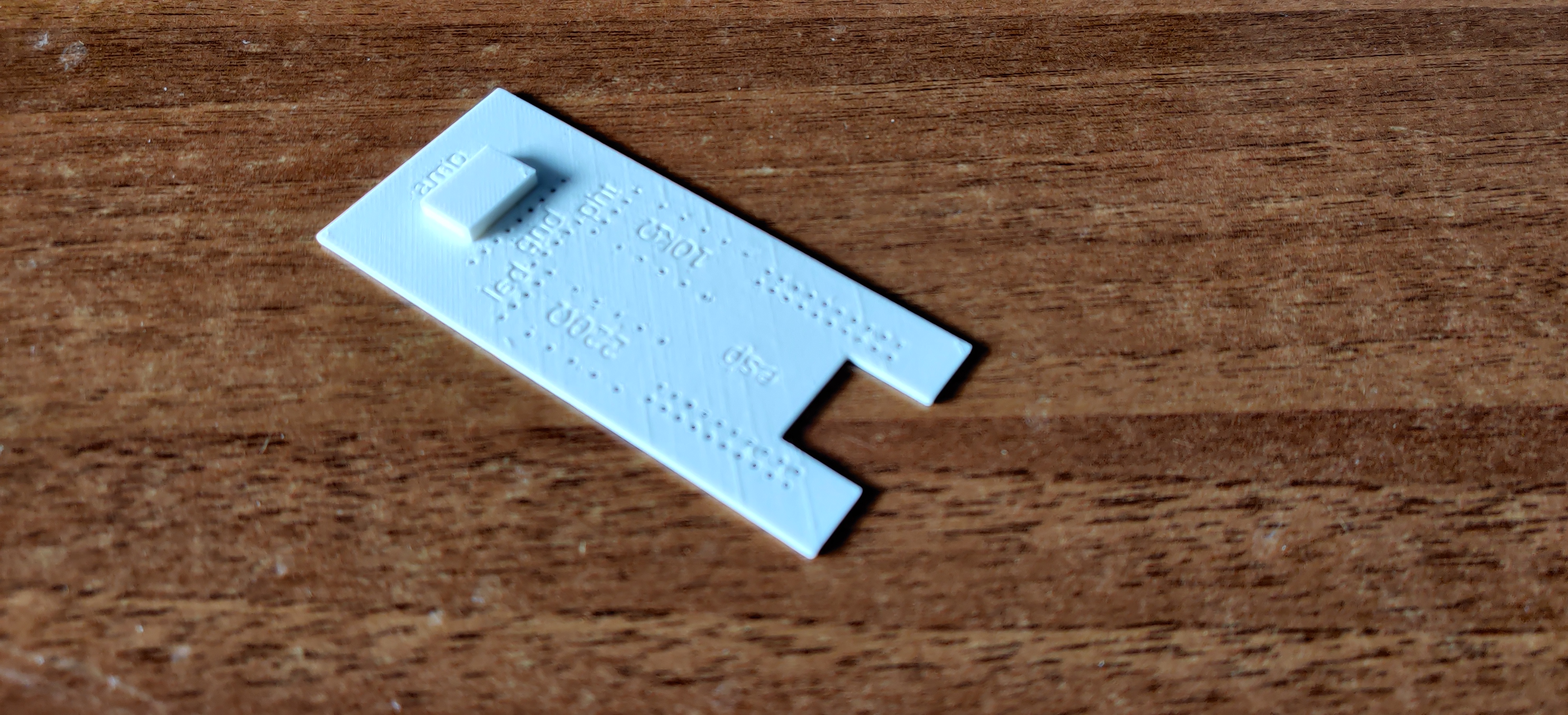 white plastic 3D-printed rectangle, with two groups of 10x2
holes around a label "esp", two groups of 5×2 holes around
labels "220Ω" and "10kΩ", three groups of 5 holes beside
labels "led", "gnd", "pht", and one group of 9 holes beside a
label "amp"; there is a notch in the rectangle near the "esp"
label, and a small raised block near the "amp" label