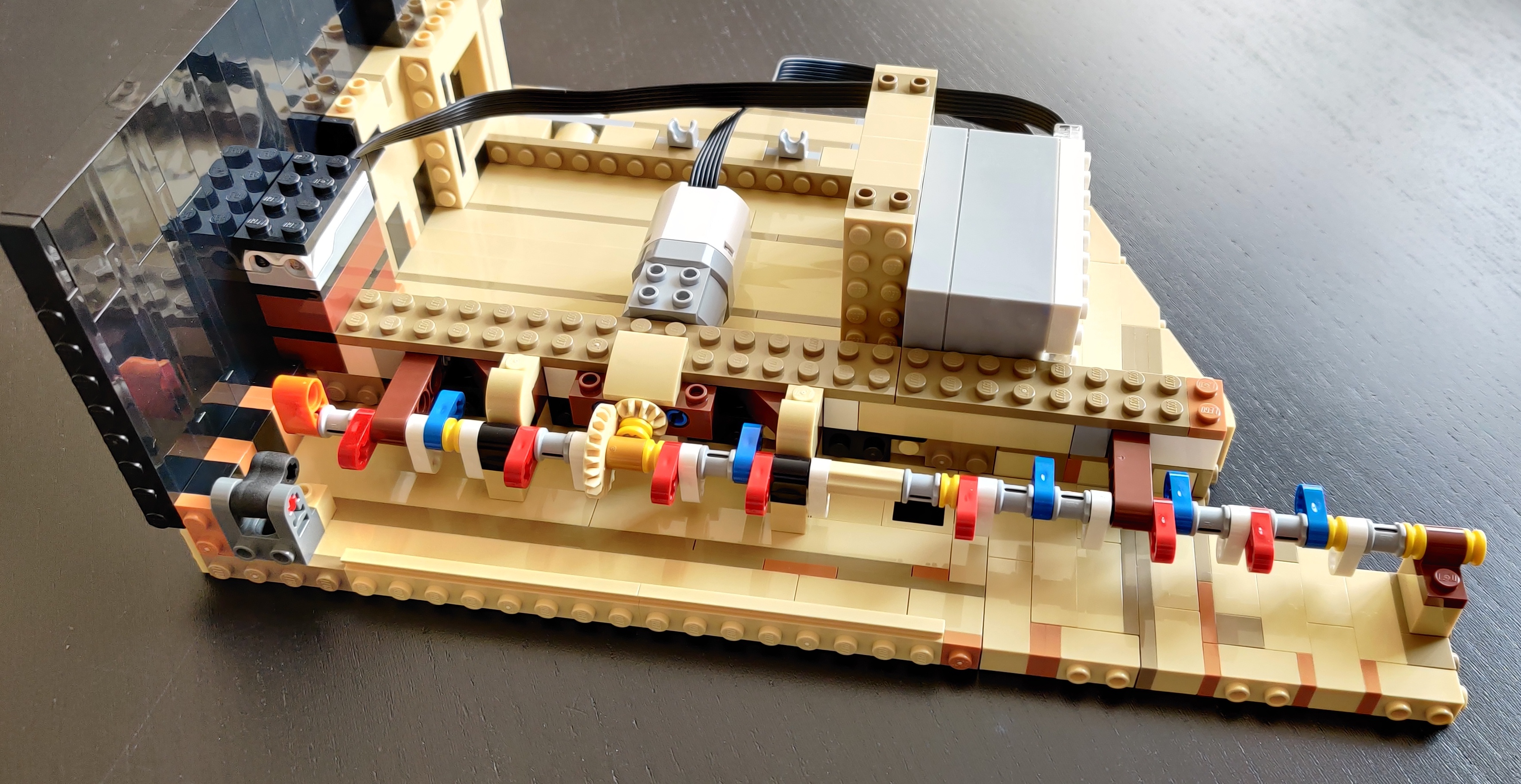 un sensore ottico Lego, motore, e scatola di controllo,
su una larga base di pezzi montati di lato; il motore fa girare
un lungo asse con camme ortogonali