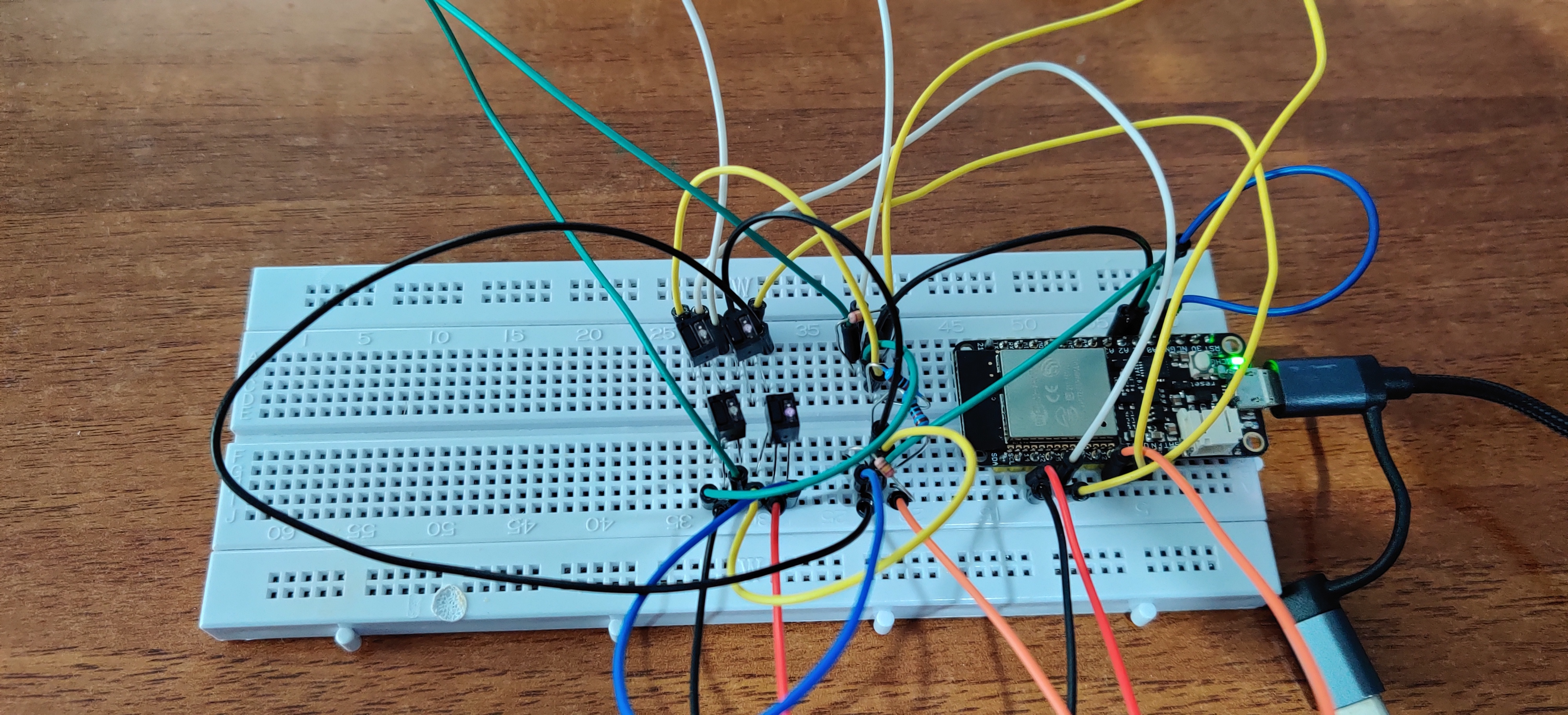 breadboard with a ESP32 dev board, 4 QRD1114 sensors, four
resistors, and a bunch of wires. One QRD1114's LED is shining
a weak pink, the others are off