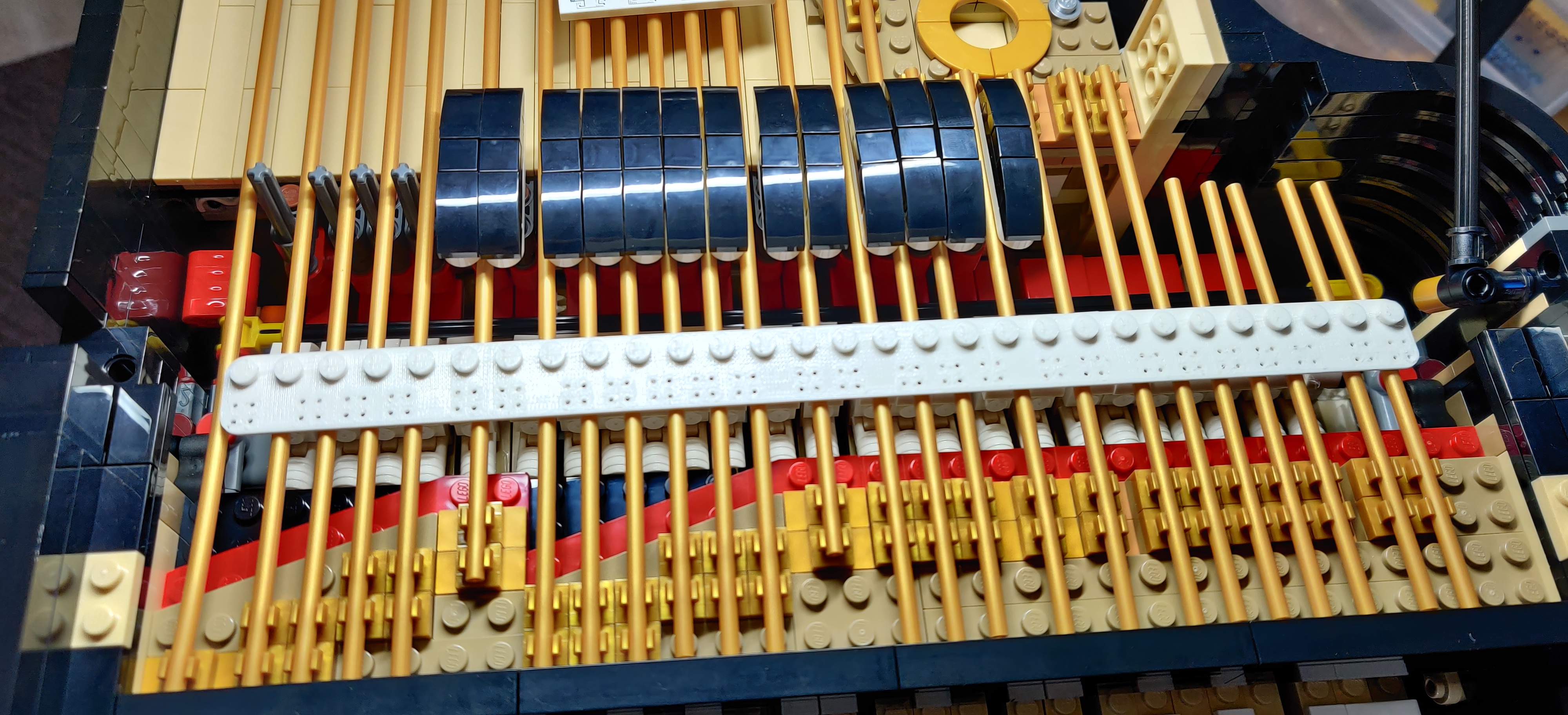 white plastic 3D-printer rectangle, 29×2 Lego studs in size,
with 25 groups of 4 small holes to hold the sensors, placed
on top of the "strings" on the piano, showing how the holes
for the sensors align with the hammers