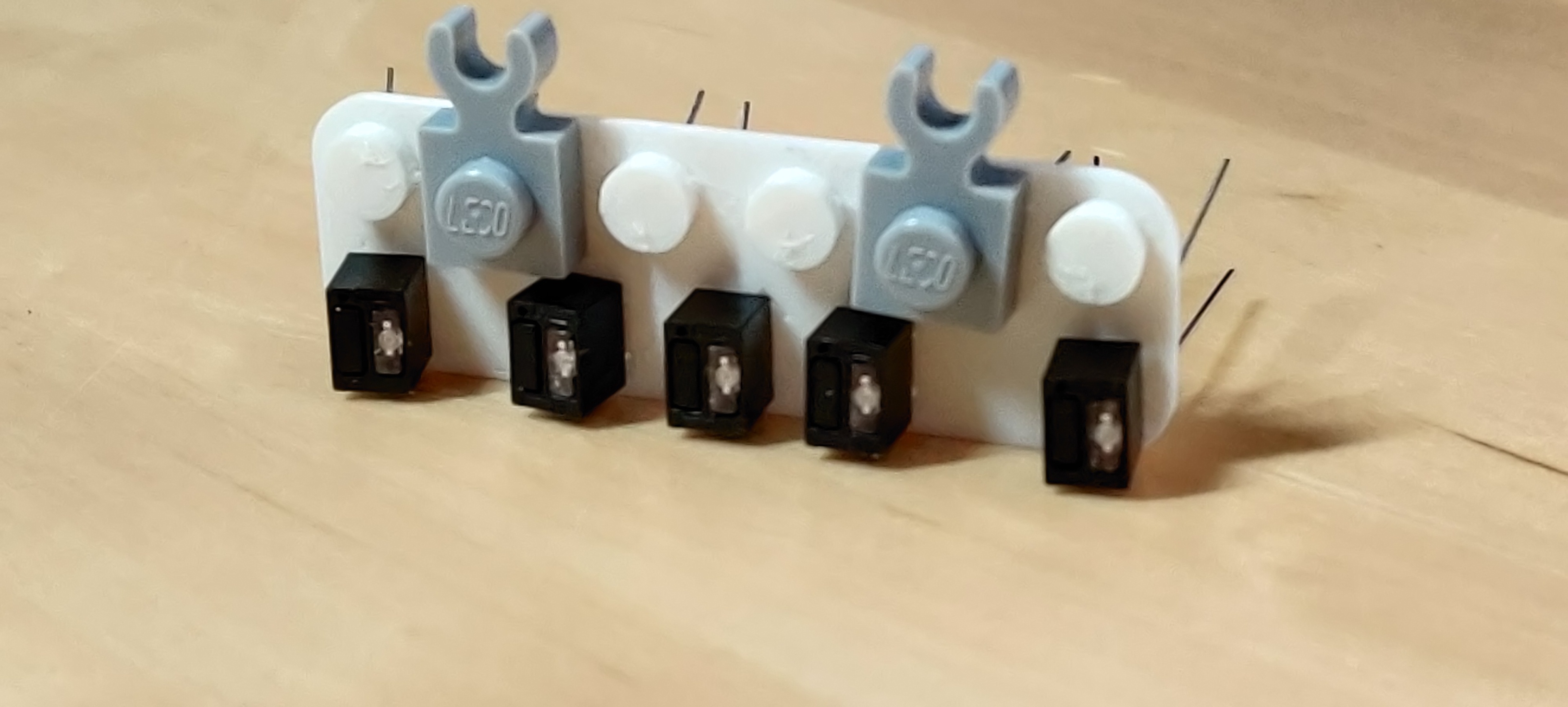 white plastic 3D-printed rectangle, 6×2 Lego studs in size,
with standard-sized studs only along one long side; 5 QRD1114
sensors occupy one long side, and 2 Lego 1×1 plates with C
clip are on the other side